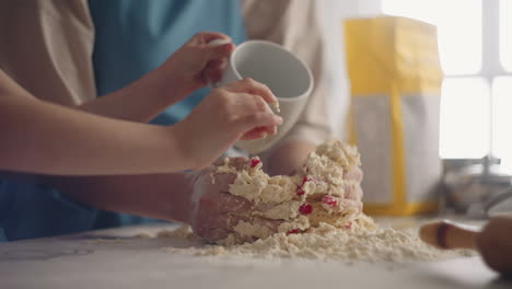woman-is-kneading-dough-on-kitchen-table-and-her-child-is-helping-little-girl-is-pouring-water-closeup-view